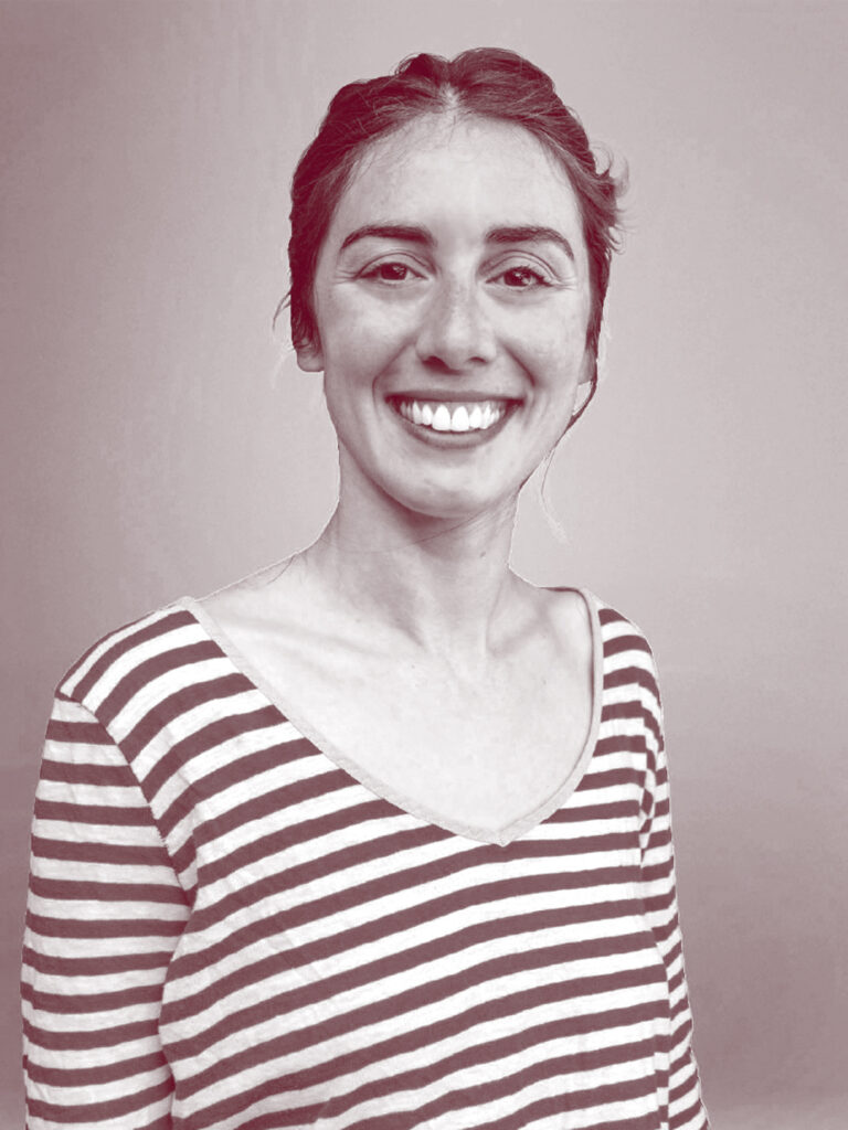 In primo piano Ginevra Bocconcelli, una donna sorridente con i capelli lisci, lunghi e raccolti dietro alla testa. Indossa una maglietta a righe sottili con scollo a V e maniche lunghe. Foto di Carlotta Stracchi Villa