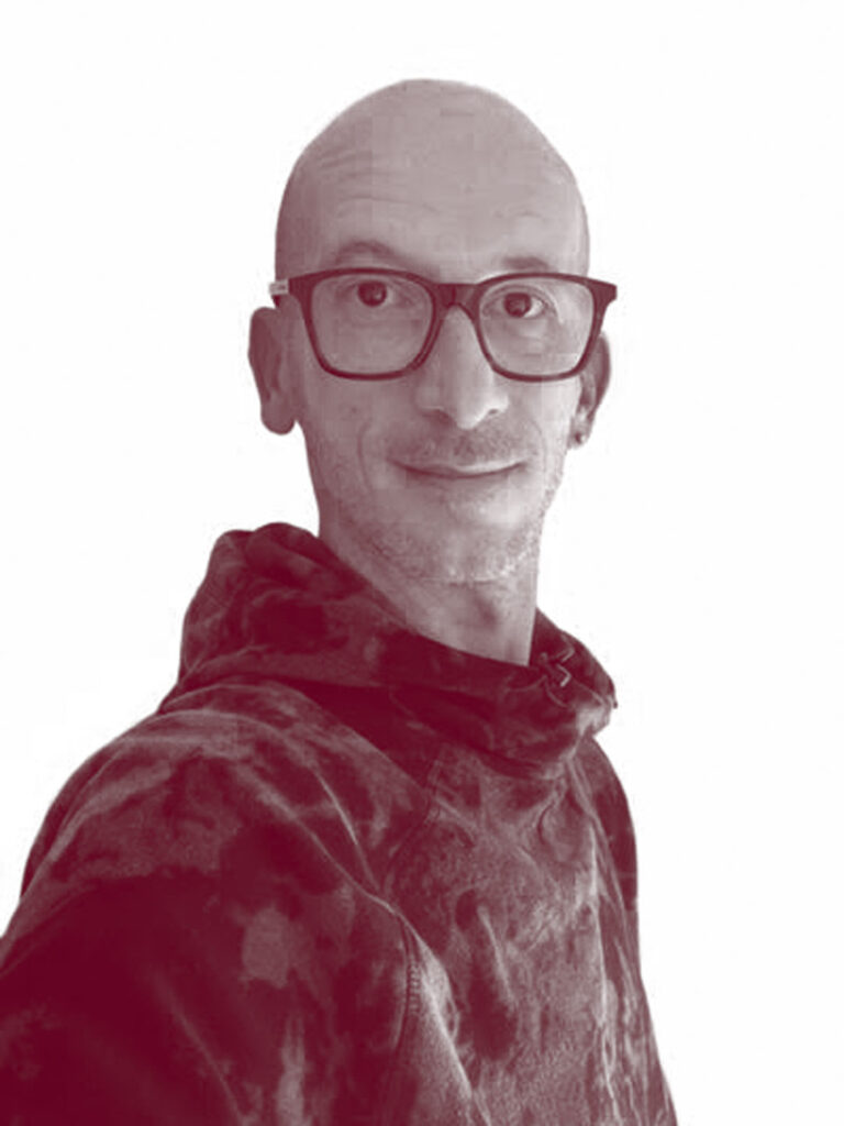 In primo piano Matteo Pedrazzi, una persona senza capelli, occhi scuri e occhiali. Indossa una felpa scura con il collo.
