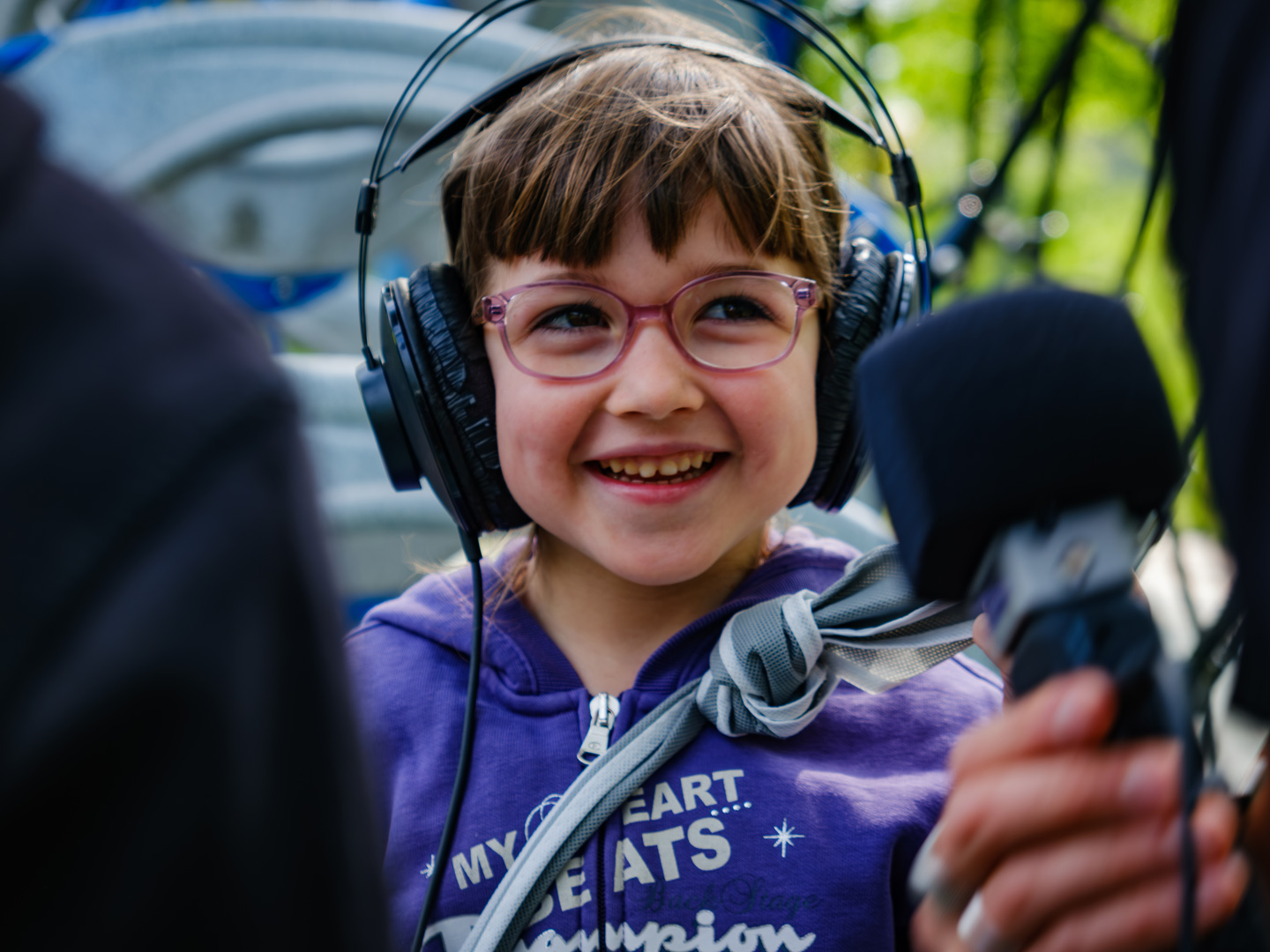 In primo piano una bambina con gli occhiali, i capelli castani con la frangetta, una felpa viola e un paio di cuffie sulla testa, sorride divertita. Foto di Carlotta Stracchi Villa.
